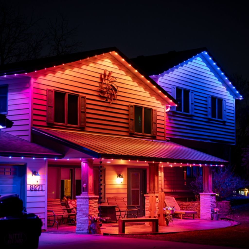 Two-story home at night with warm orange and deep blue gables and a porch washed in magenta downlight