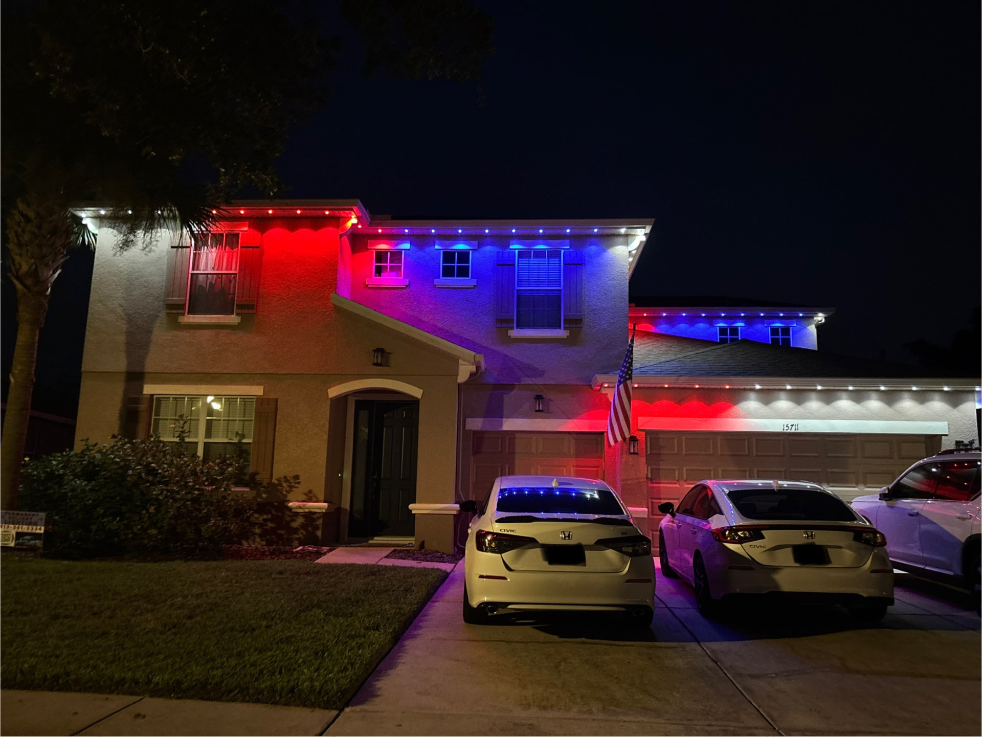 Stucco home at night lit in red, white and blue permanent soffit light along the upper and lower fascia