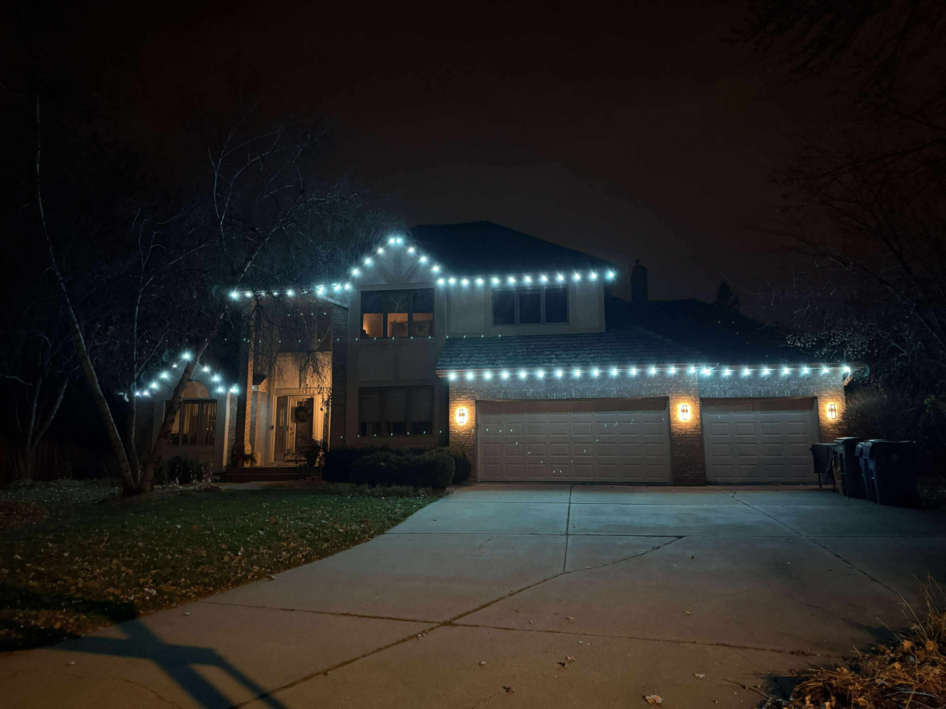 Two-story home at night with crisp white permanent LED lights tracing the roof gables, gutters and garage roofline