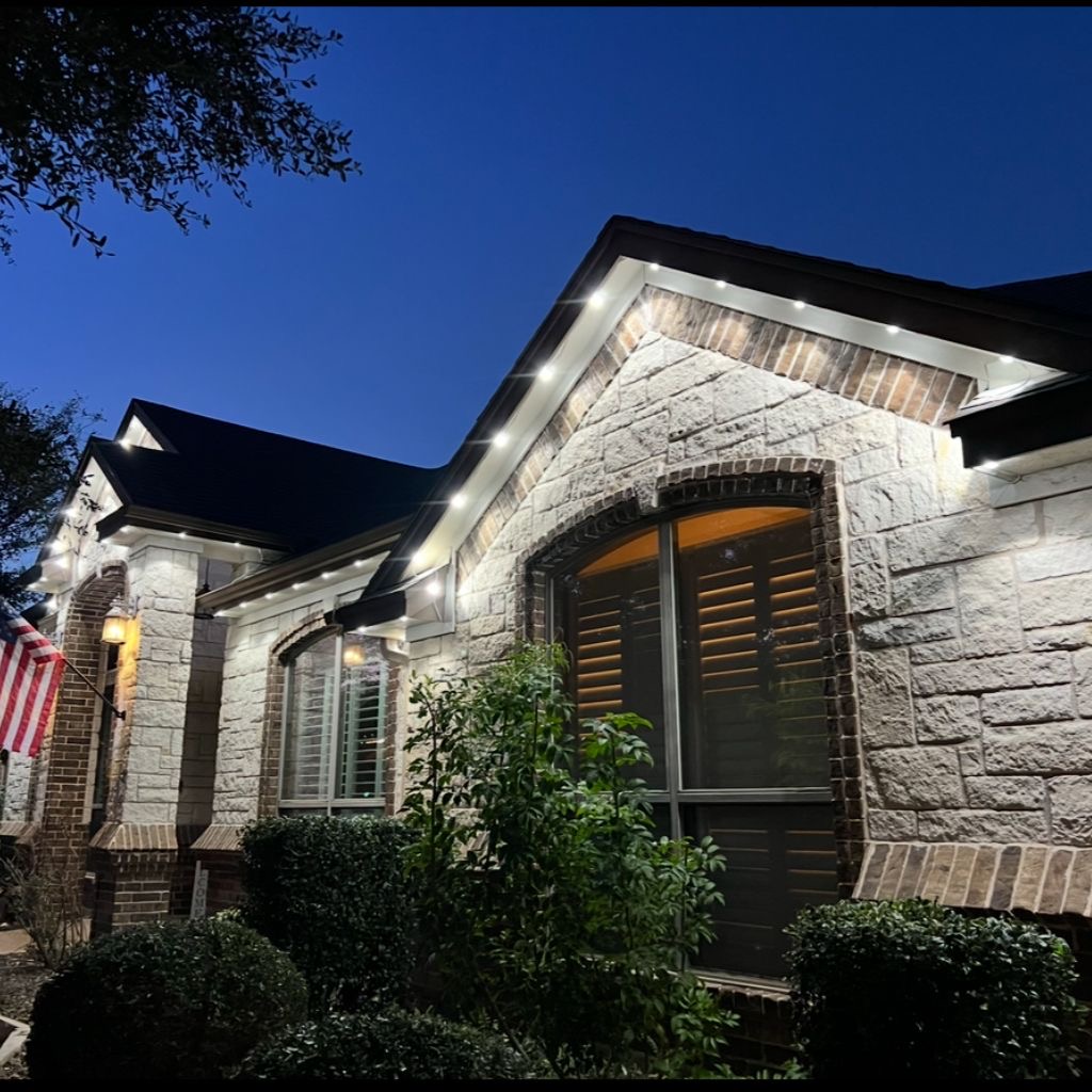 Rustic stone facade at dusk with warm soffit downlights washing the masonry under the eaves