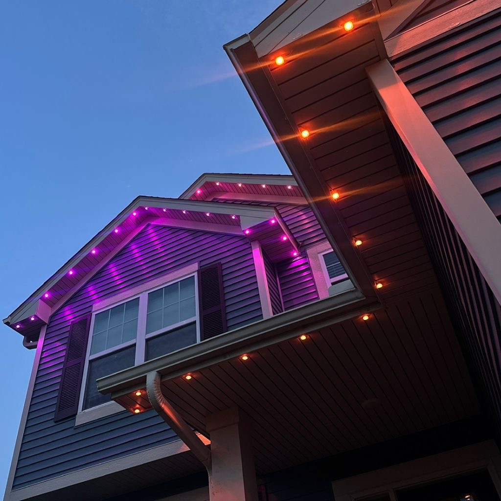 Low-angle dusk view of siding and porch soffits glowing purple above warm amber downlights